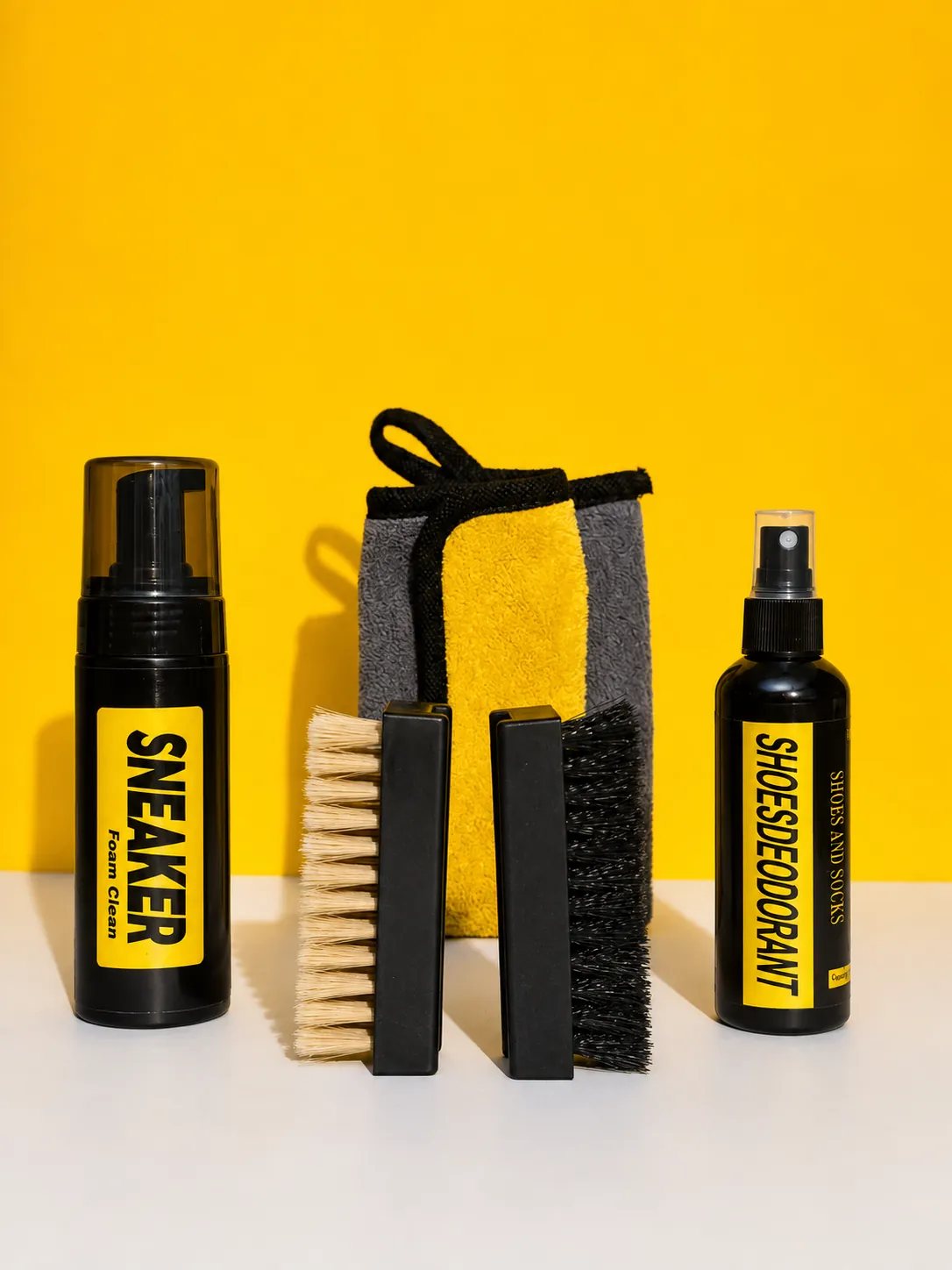 Kit CleanStep completo: Foam Clean, dos cepillos, toalla de microfibra y Shoe Deodorant sobre fondo amarillo